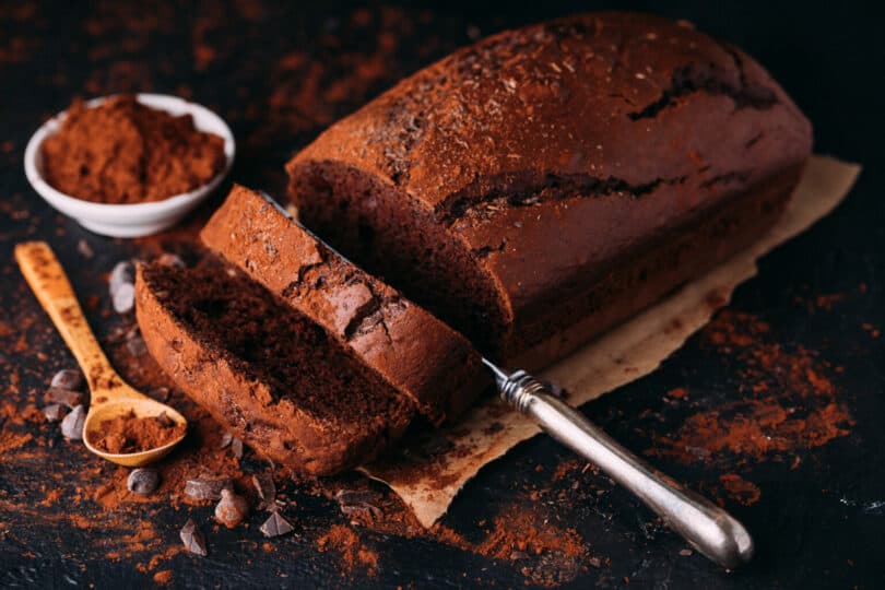 Schokoladenkuchen auf dunklem Untergrund, neben Messer und Kakao, Metapher für Rezepte und Führungstechniken.